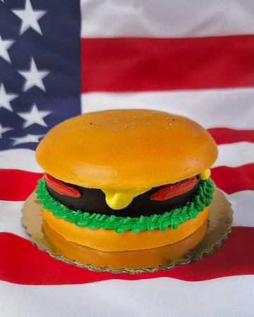 Hamburger-shaped cake on a stand with an American flag in the background