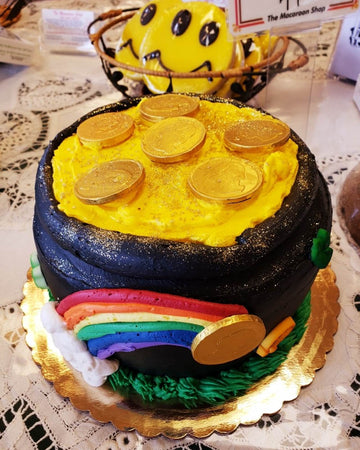 Colorful cake with gold coins, rainbow, and pot of gold on a decorative plate.