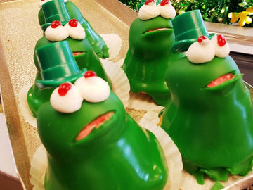 Green character figurines with white faces and red noses on a reflective surface.