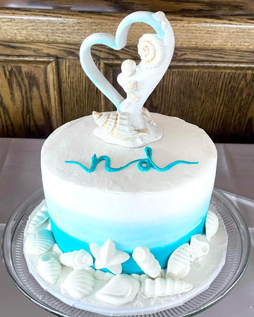 Two-tiered cake with blue and white color scheme, decorative elements, and a heart-shaped topper.