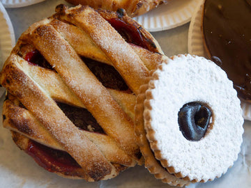 Close-up of a lattice-topped pie and a round cookie with a dark center on a light surface.