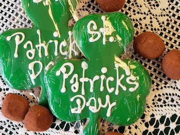 Green St. Patrick's Day cookies shaped like shamrocks on a lace tablecloth.