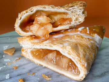 Two apple turnovers stacked on a marble surface with an orange background